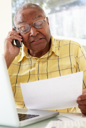 An older man reviews his personal insurance plan's paperwork while calling his insurer.