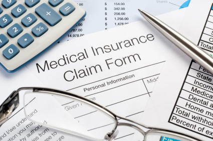 A medical insurance claim form sits on a desk with a pair of glasses and a pen waiting to be completed. 