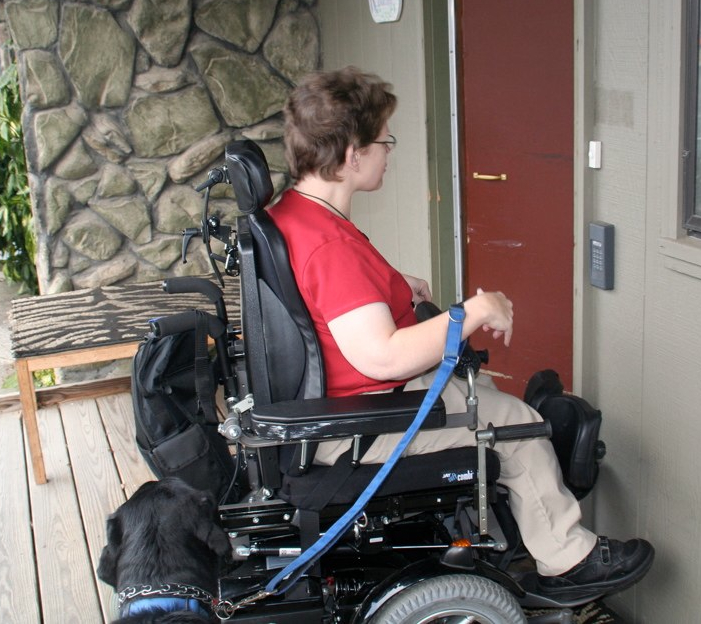 A woman enters her front door in her wheelchair with her guide dog.